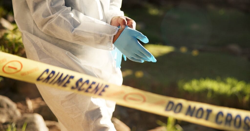 Forensic gloves and police tape at a crime scene, indicating an investigation setup with hazmat preparation in progress.